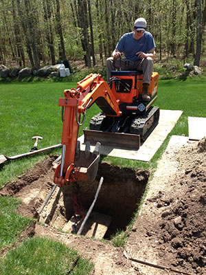 Using a mini-excavator to work on a small area, a Grenco team member removes dirt and puts it in a neat pile.